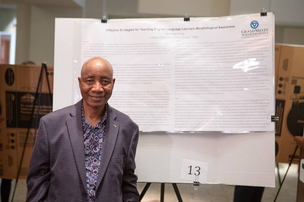 Literacy studies faculty member, Dr. Nagnon Diarrasouba, standing in front of literacy studies graduate student, Maximilian Young's, poster.